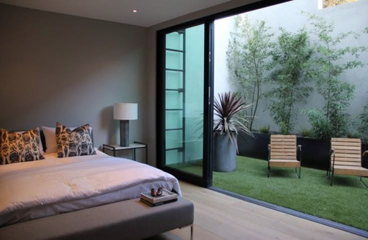 a white bed sitting in a bedroom next to a sliding glass door that opens onto a lush green yard