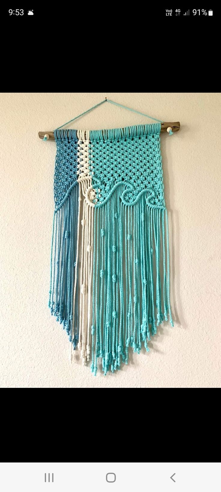 a blue wall hanging with fringes and beads on the bottom, in front of a white wall