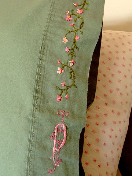 a close up of a pillow on a bed with embroidered flowers and an o - ring