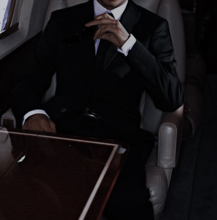 a man in a tuxedo sitting at a desk with his hand on his chin