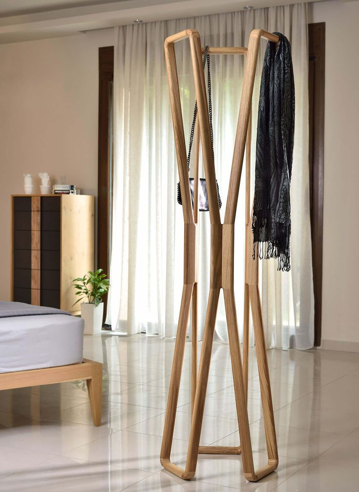 a wooden coat rack in the middle of a room next to a bed and window