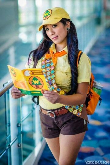 a woman in short shorts and a yellow hat is holding a book while looking at the camera