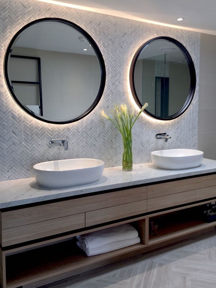 two round mirrors on the wall in a bathroom with double sinks and large mirror above them