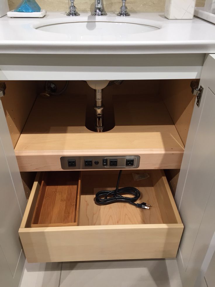 an open drawer in a bathroom with a sink and counter top behind it, under which is a power strip