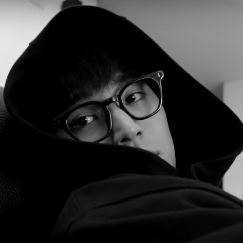 a young man wearing glasses and a hoodie looking at the camera while sitting on a couch