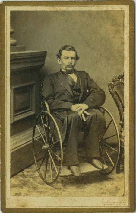 an old time photo of a man in a suit sitting in a wheel chair with his legs crossed