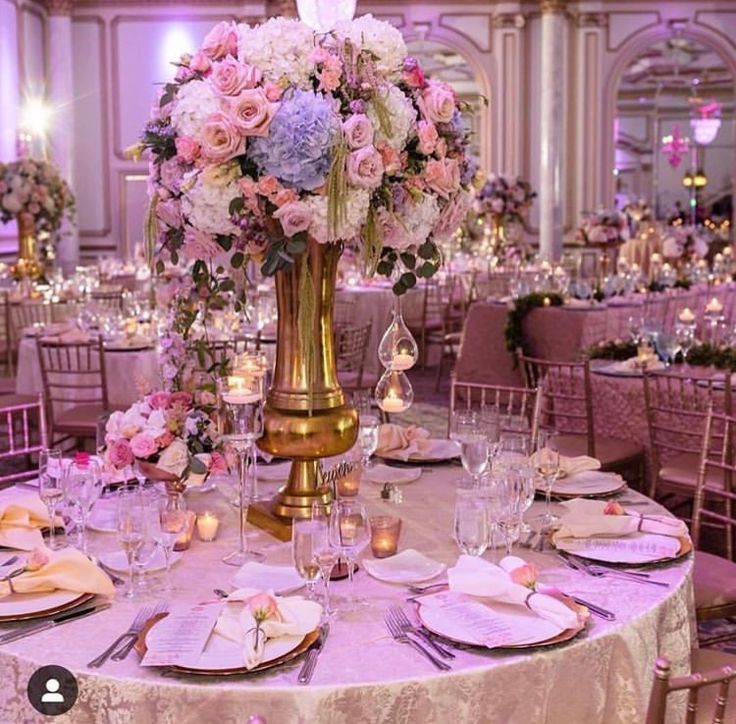 a table set up with pink and white flowers in a tall gold vase on top