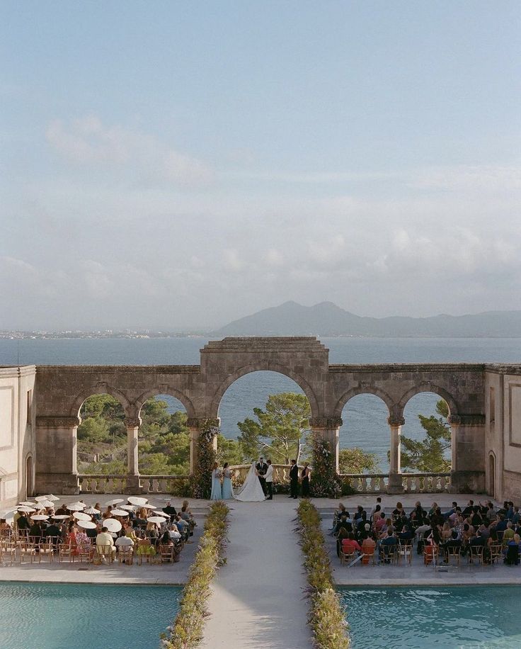 an outdoor ceremony is set up in front of the water and people are sitting at tables under umbrellas