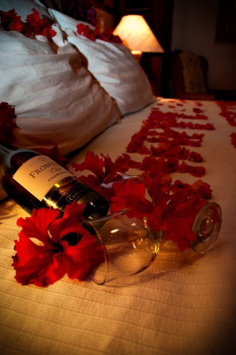 a bottle of wine sitting on top of a bed next to a vase filled with red flowers