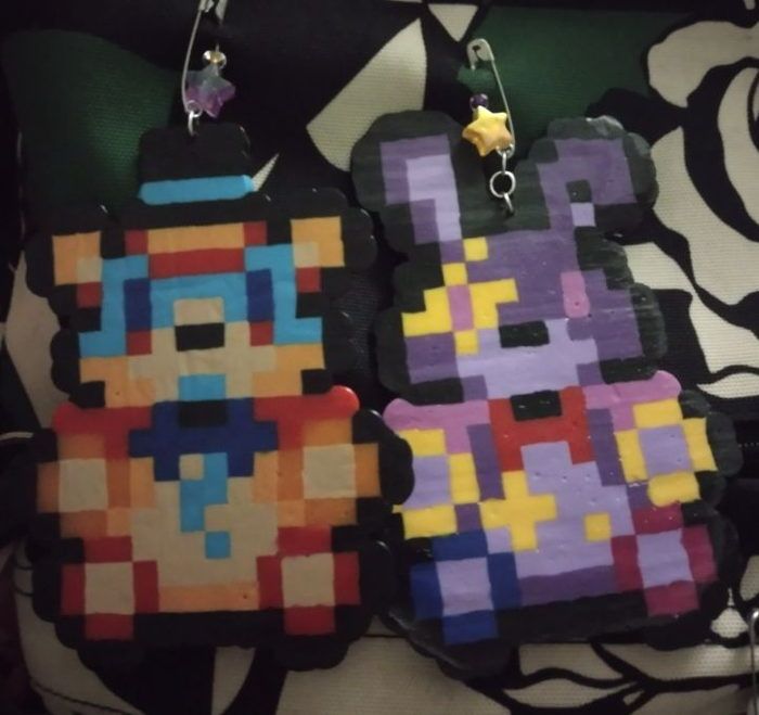 two earrings made to look like video games characters are hanging on a black and white pillow