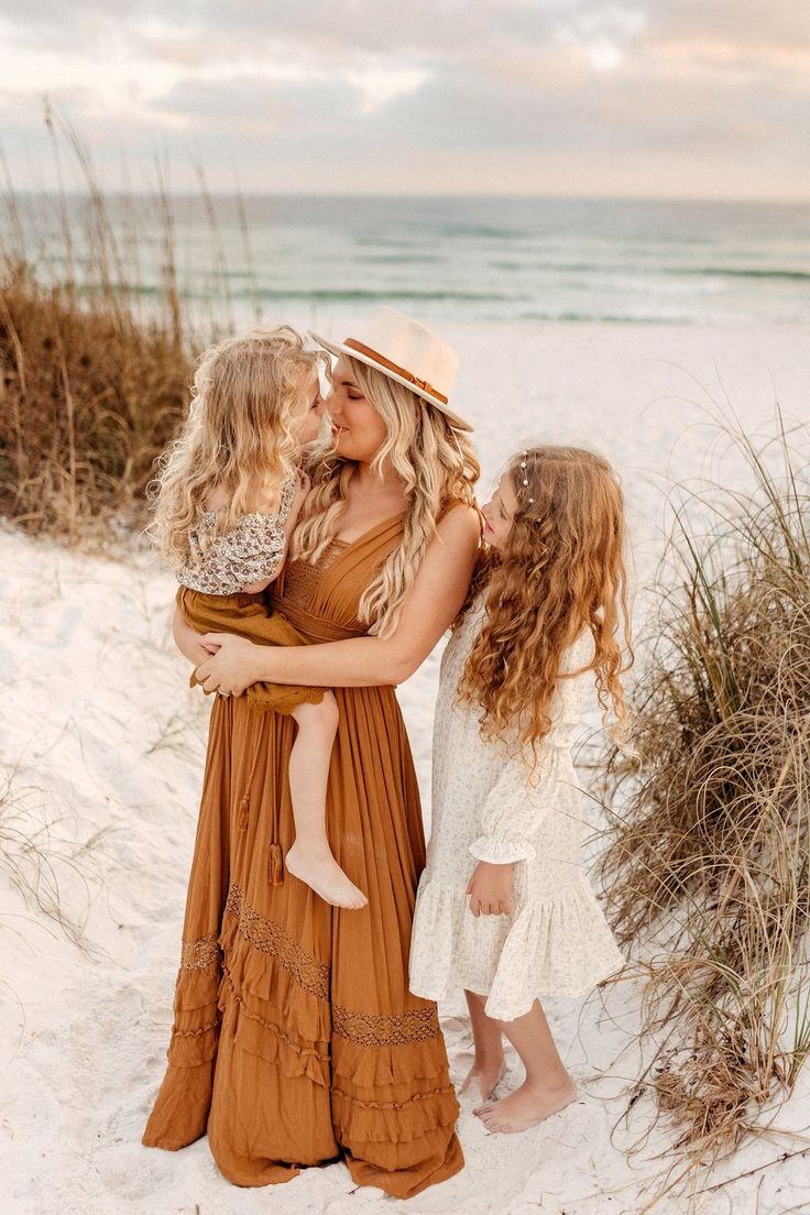 three girls are standing on the beach and hugging each other while one girl is holding her baby