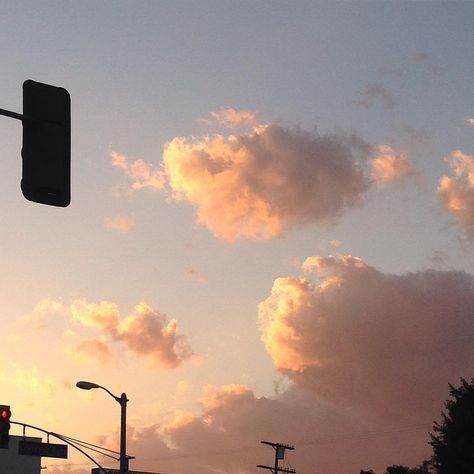 the sun is setting behind some clouds in the sky over a street light and traffic signal