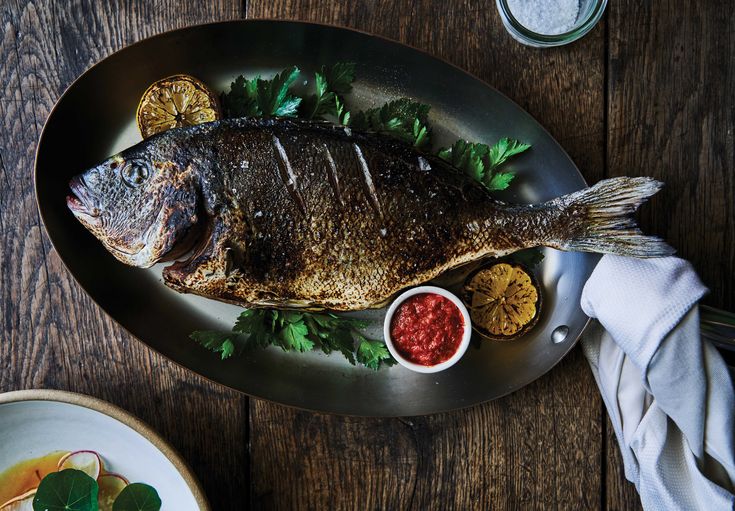 a fish is sitting on a plate with sauces and other food items around it