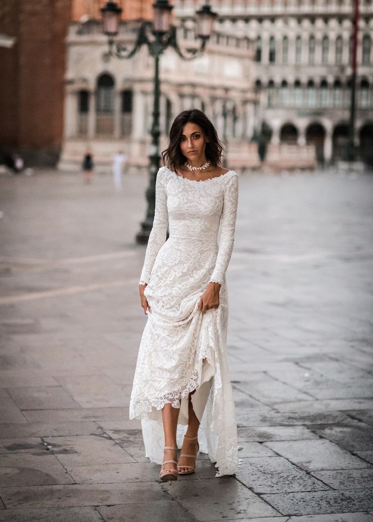 a woman in a white dress is standing on the street with her hands behind her back