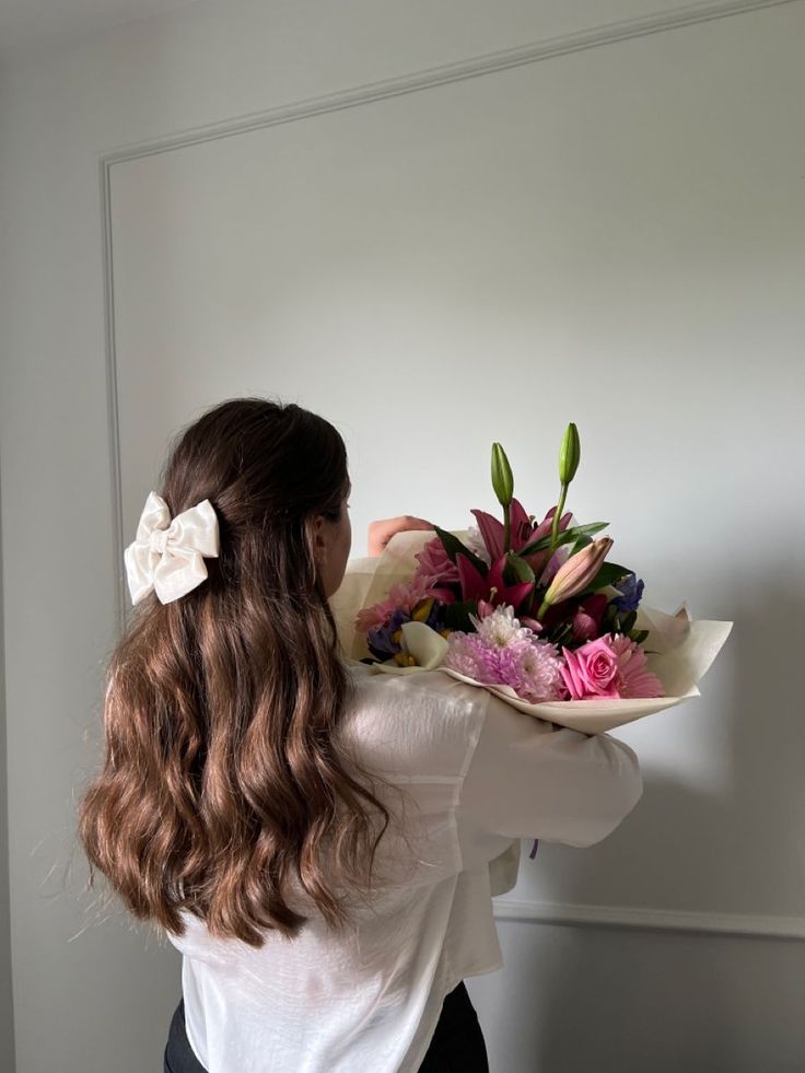 a woman holding a bouquet of flowers in front of her face and looking at the wall