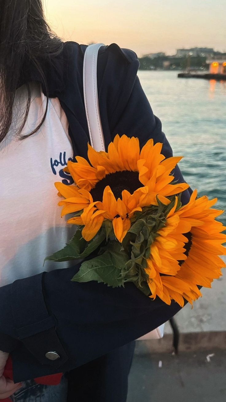 a woman holding a bouquet of sunflowers in front of a body of water