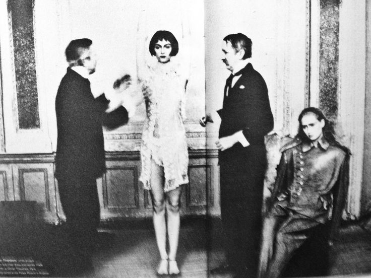 an old black and white photo of three people standing in front of a woman wearing a dress