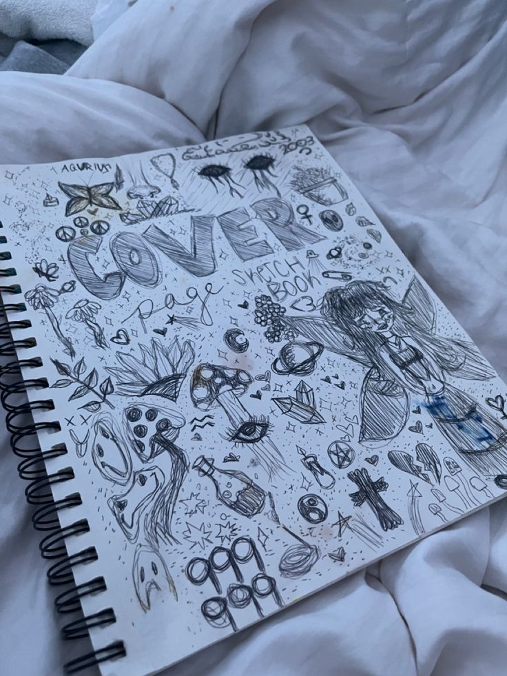 an open notebook sitting on top of a bed covered in white sheets and blankets with drawings