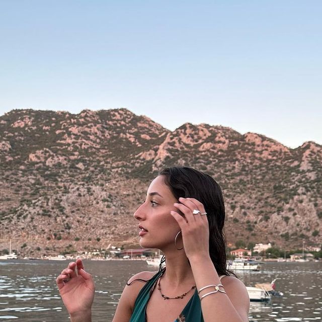 a woman in a green dress is talking on her cell phone while standing near the water