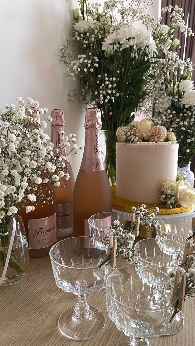 a table topped with wine glasses next to bottles and vases filled with flowers on top of a wooden table