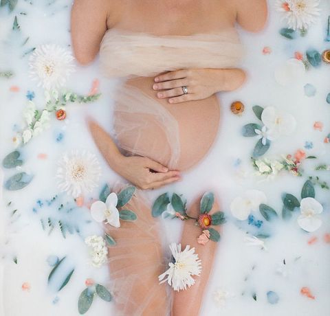 a pregnant woman laying in a bathtub surrounded by flowers and greenery with her hands on her belly