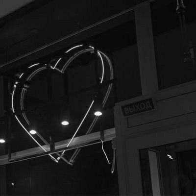 a black and white photo of a heart shaped neon sign hanging from the side of a building