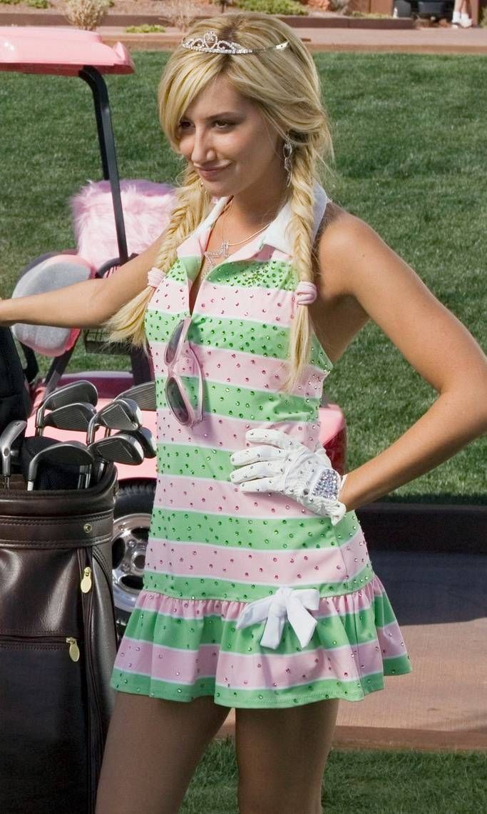 a woman in a pink and green dress holding a golf club bag while standing next to a cart