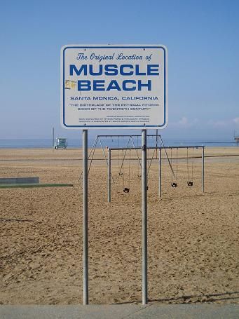 there is a sign that says muscle beach in front of the grass and dirt field