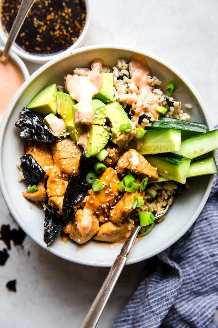 a white bowl filled with chicken, rice and cucumbers