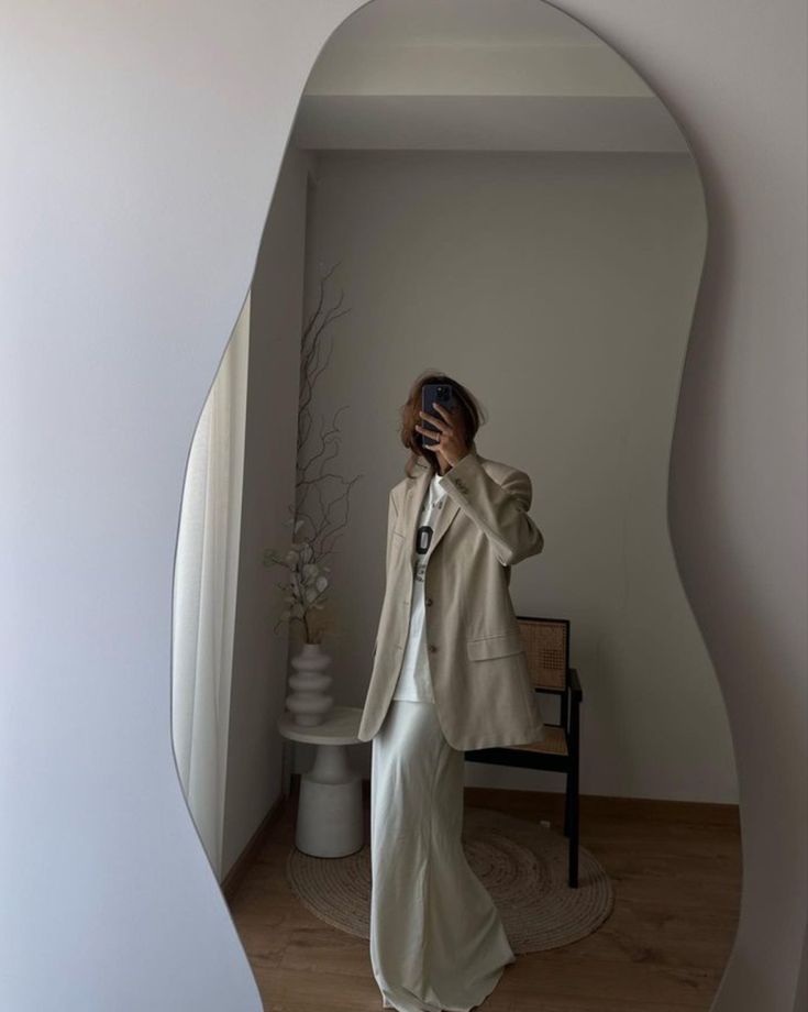 a woman in a white dress is taking a selfie with her cell phone while wearing a beige blazer