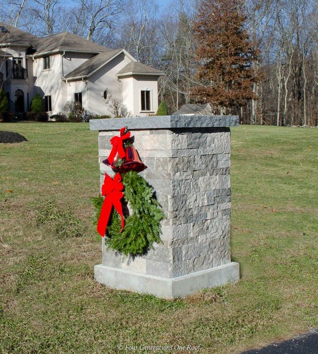 a christmas wreath on top of a stone pillar in front of a house with a red bow