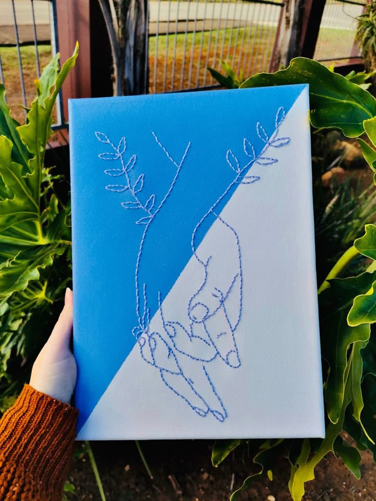 a person holding up a blue and white canvas with an image of someone's hand on it