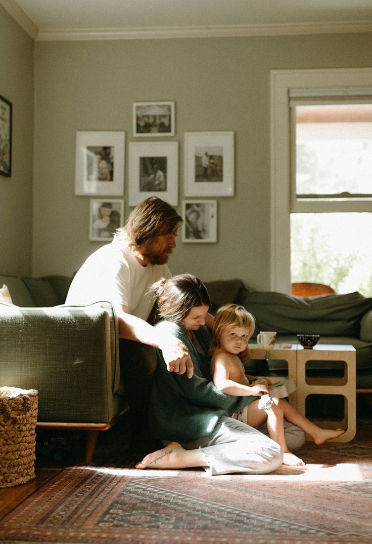 a man and two children sitting on the floor in front of a couch next to a coffee table