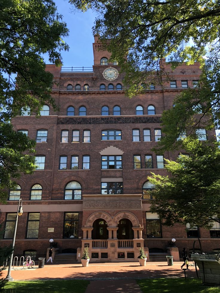 an old brick building with a clock on the top of it's face and trees in front