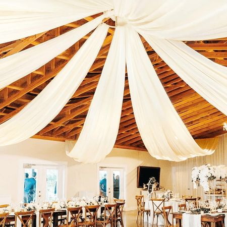 the inside of a wedding reception with white draping on the ceiling and tables