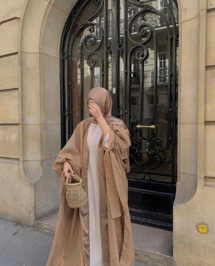 a woman in a brown shawl is walking down the street with her hand on her face