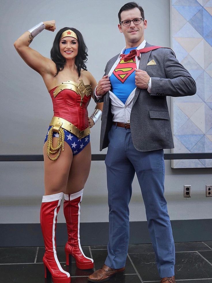 a man standing next to a woman dressed as wonder and superman in front of a wall