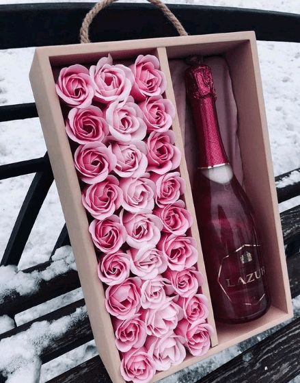 a box with pink roses and a bottle in it sitting on a wooden bench covered in snow