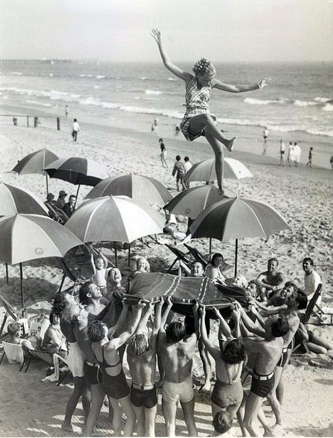 a woman is balancing on top of umbrellas at the beach while others are in the water