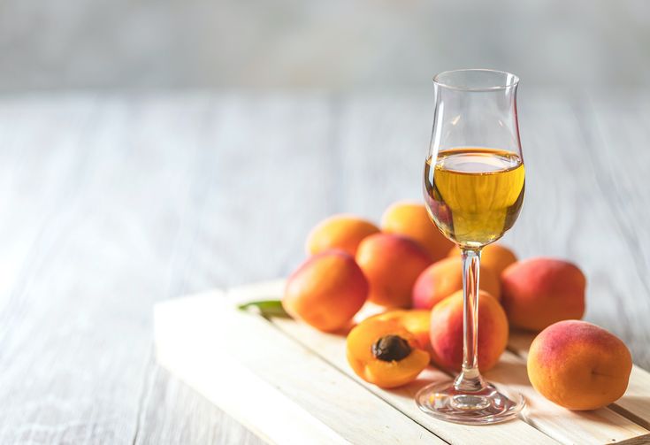 a glass of wine sitting on top of a wooden table next to peaches and oranges