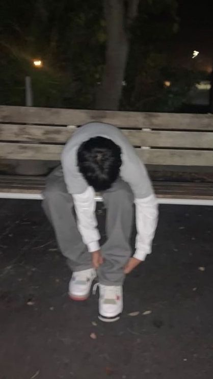 a person sitting on a park bench with their head in the ground while wearing sneakers