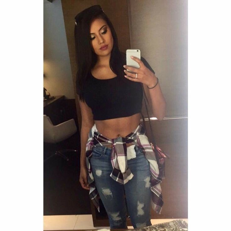 a woman standing in front of a mirror holding a cell phone and wearing ripped jeans