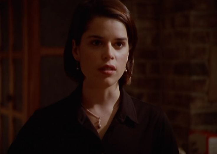 a woman standing in front of a brick wall wearing a black shirt and silver necklace