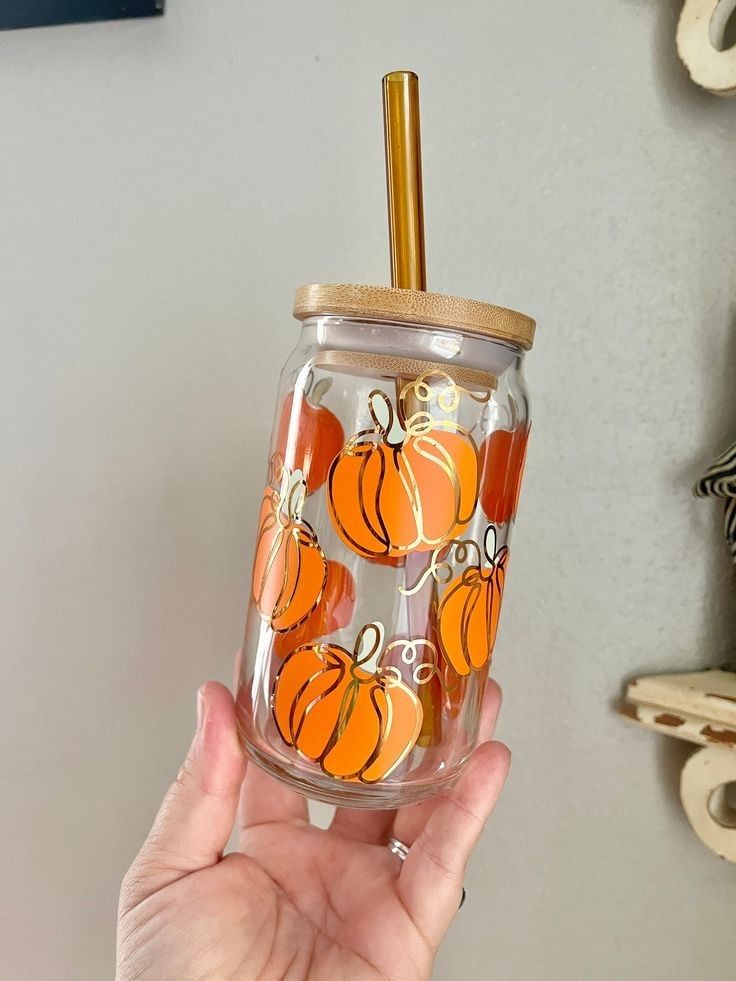 a hand holding a glass with pumpkins painted on it and a gold straw in the top