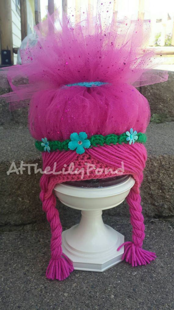 a pink hat on top of a white pedestal with green flowers in the center and purple yarn around it