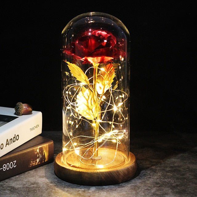 a rose in a glass jar with fairy lights on it next to a stack of books