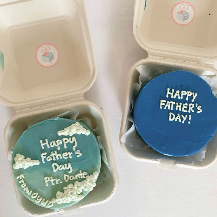 two birthday cakes in plastic containers with happy father's day written on them, one is blue and the other is green