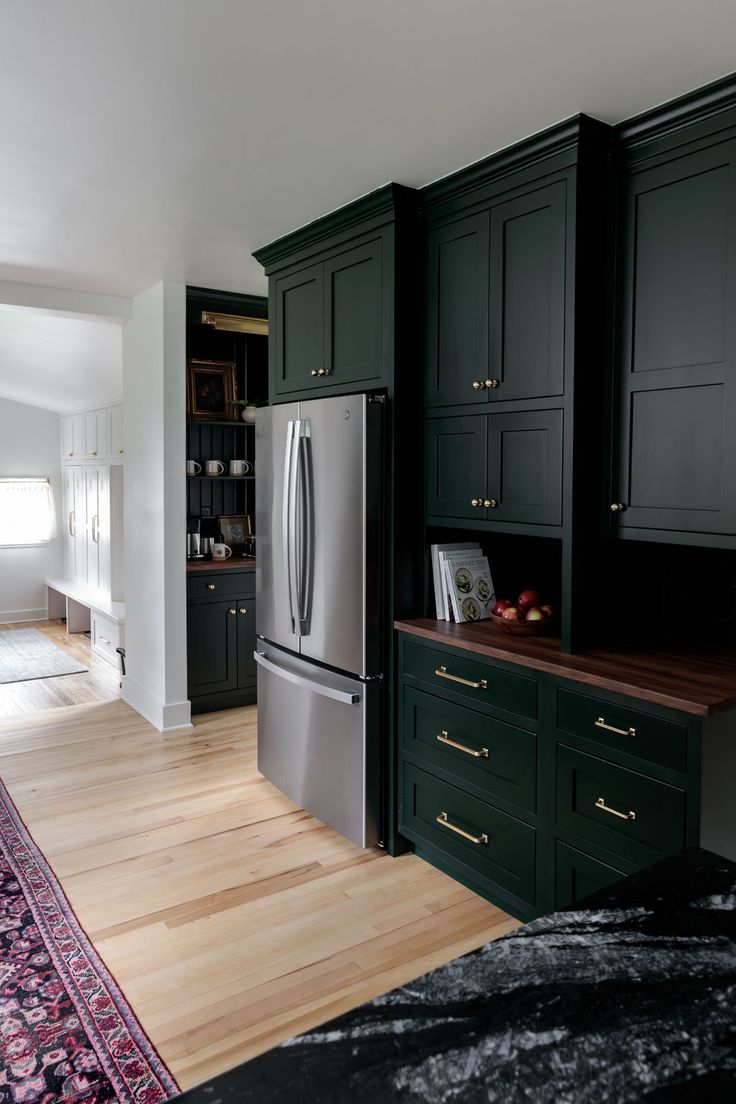 a kitchen with dark green cabinets and wood flooring on the countertop, along with a rug