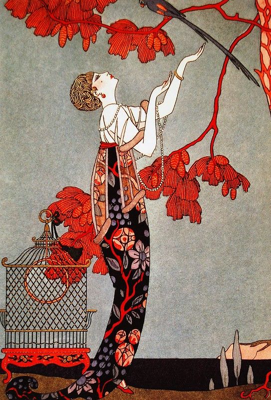 a woman holding a bird in her hand while standing under a tree with red leaves