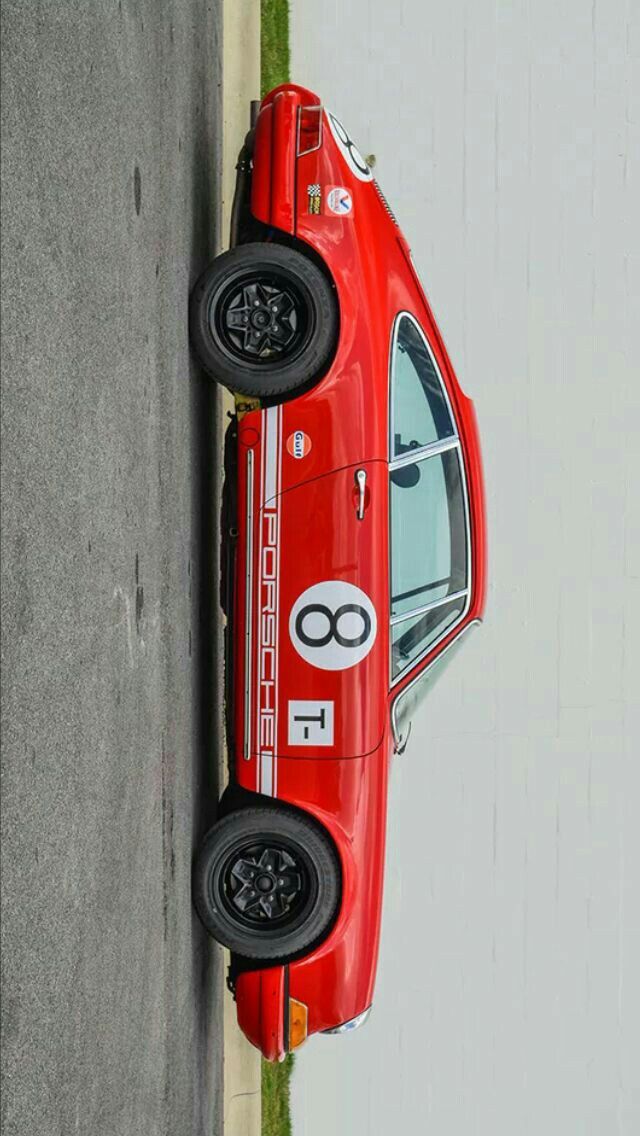 a red race car parked on the side of a road next to a white wall